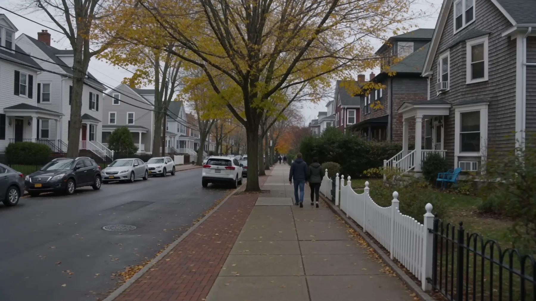 A residential street in Cambridge, Massachusetts: clapboard houses, parked cars and a brick sidewalk under autumn trees.